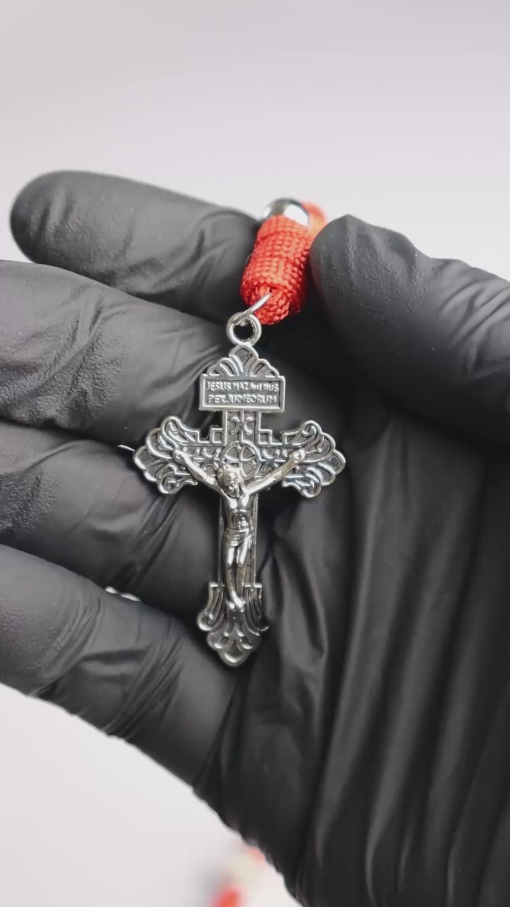 Rosario católico Sanguis Christi sostenido en la mano con cuentas metálicas y cordón rojo