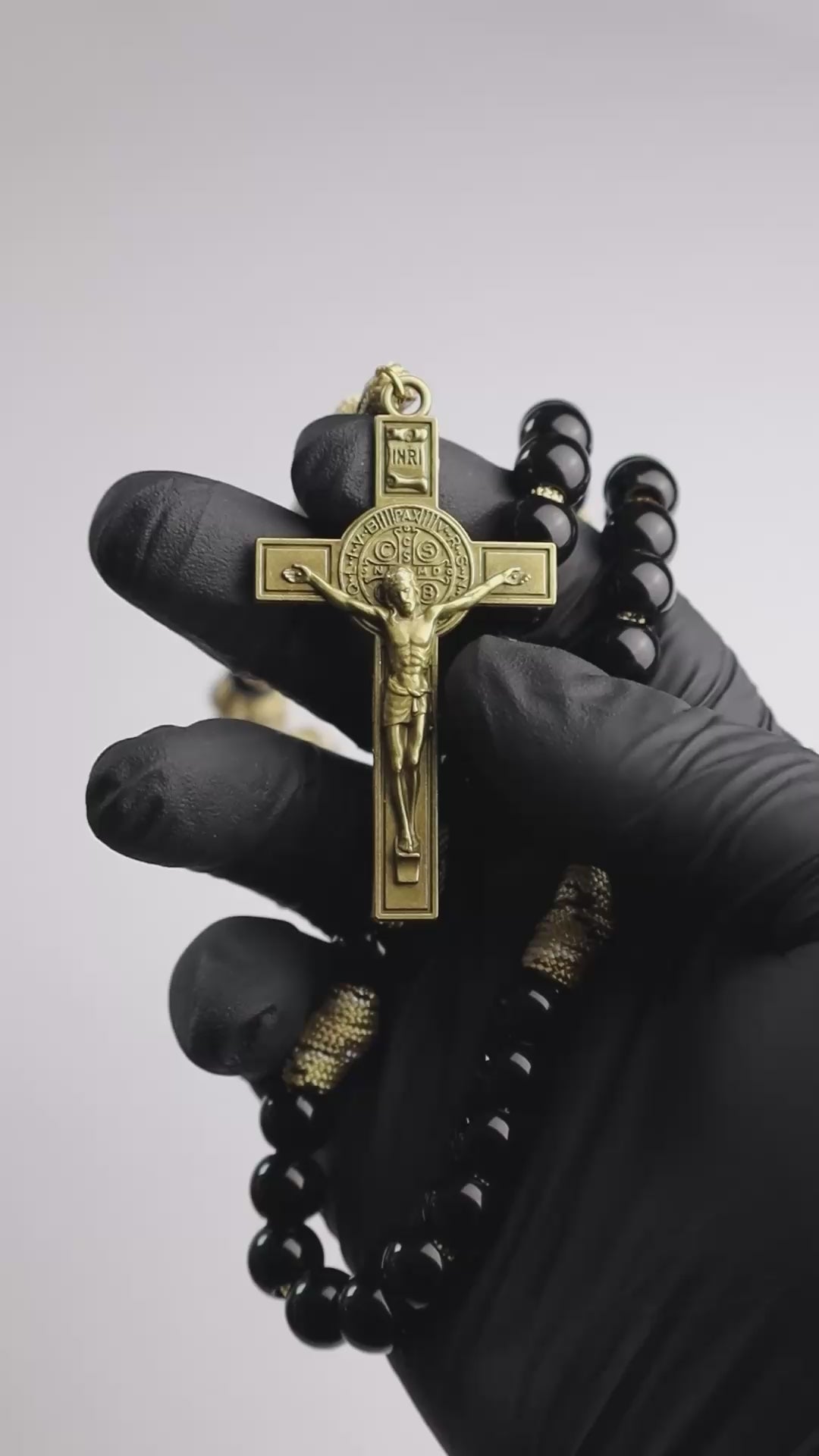 Rosario católico Lux in Tenebris sostenido en la mano con cruz dorada