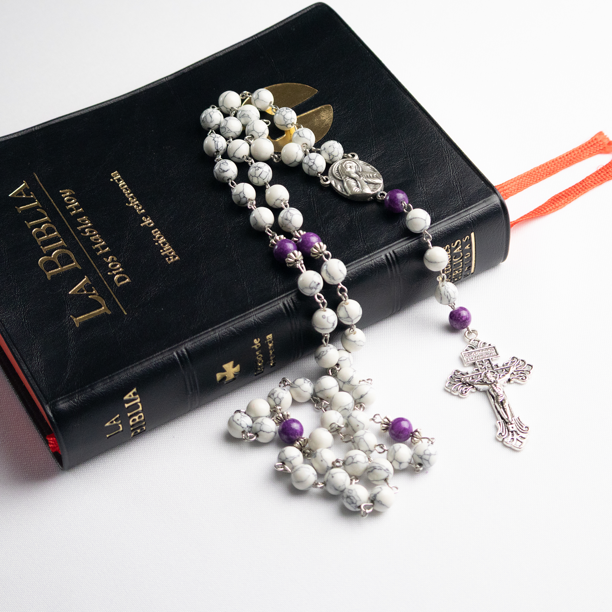 Rosario católico Mater Dolorosa sobre libro con cruz metálica y piedras naturales